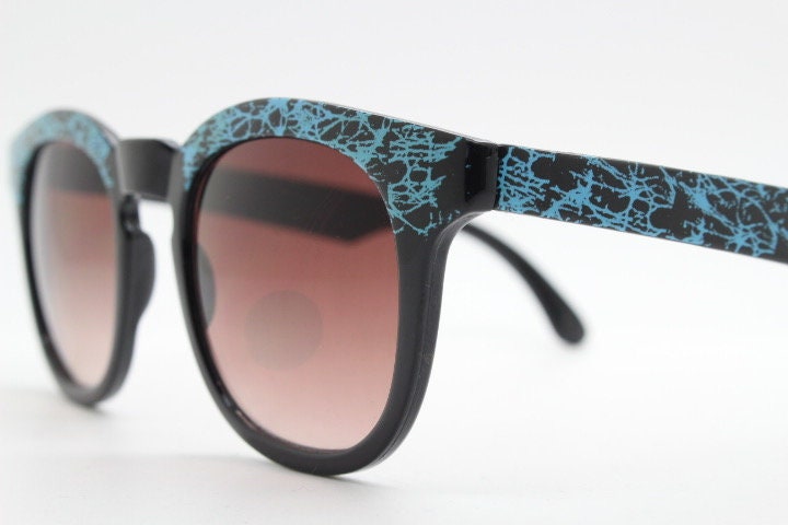 80s vintage rounded wayfarer design sunglasses. Abstract patterned blue brow and arms on a black frame with graduating lenses. Unused NOS