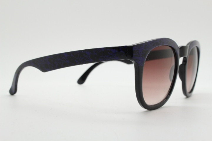 80s vintage rounded wayfarer design sunglasses. Abstract patterned purple brow and arms on a black frame with graduating lenses. Unused NOS