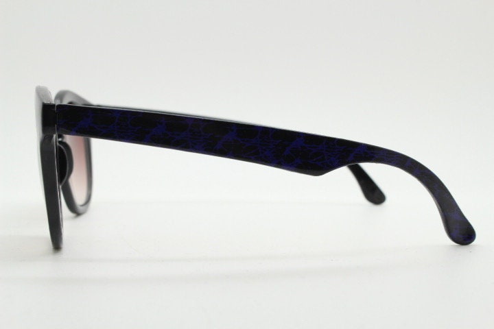80s vintage rounded wayfarer design sunglasses. Abstract patterned purple brow and arms on a black frame with graduating lenses. Unused NOS