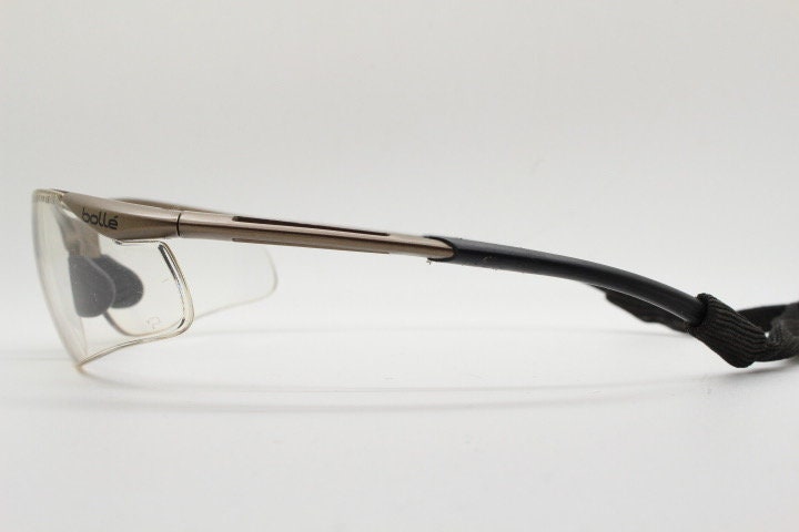 Bolle 90s vintage sports shield sunglasses. Aerodynamic clear lens wrap around half frame design in satin finish with tie string. Cycling