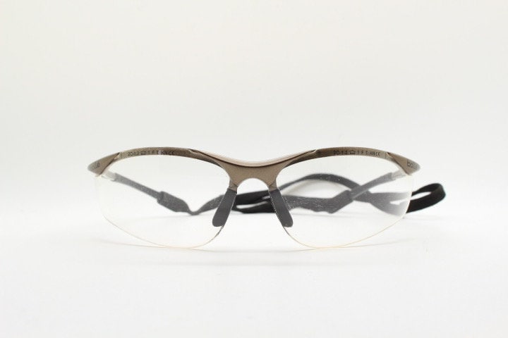 Bolle 90s vintage sports shield sunglasses. Aerodynamic clear lens wrap around half frame design in satin finish with tie string. Cycling