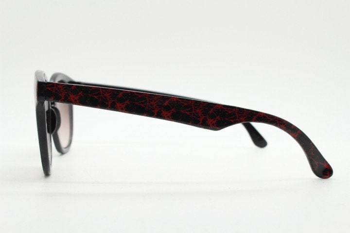 80s vintage rounded wayfarer design sunglasses. Abstract patterned red brow and arms on a black frame with graduating  lenses. Unused NOS