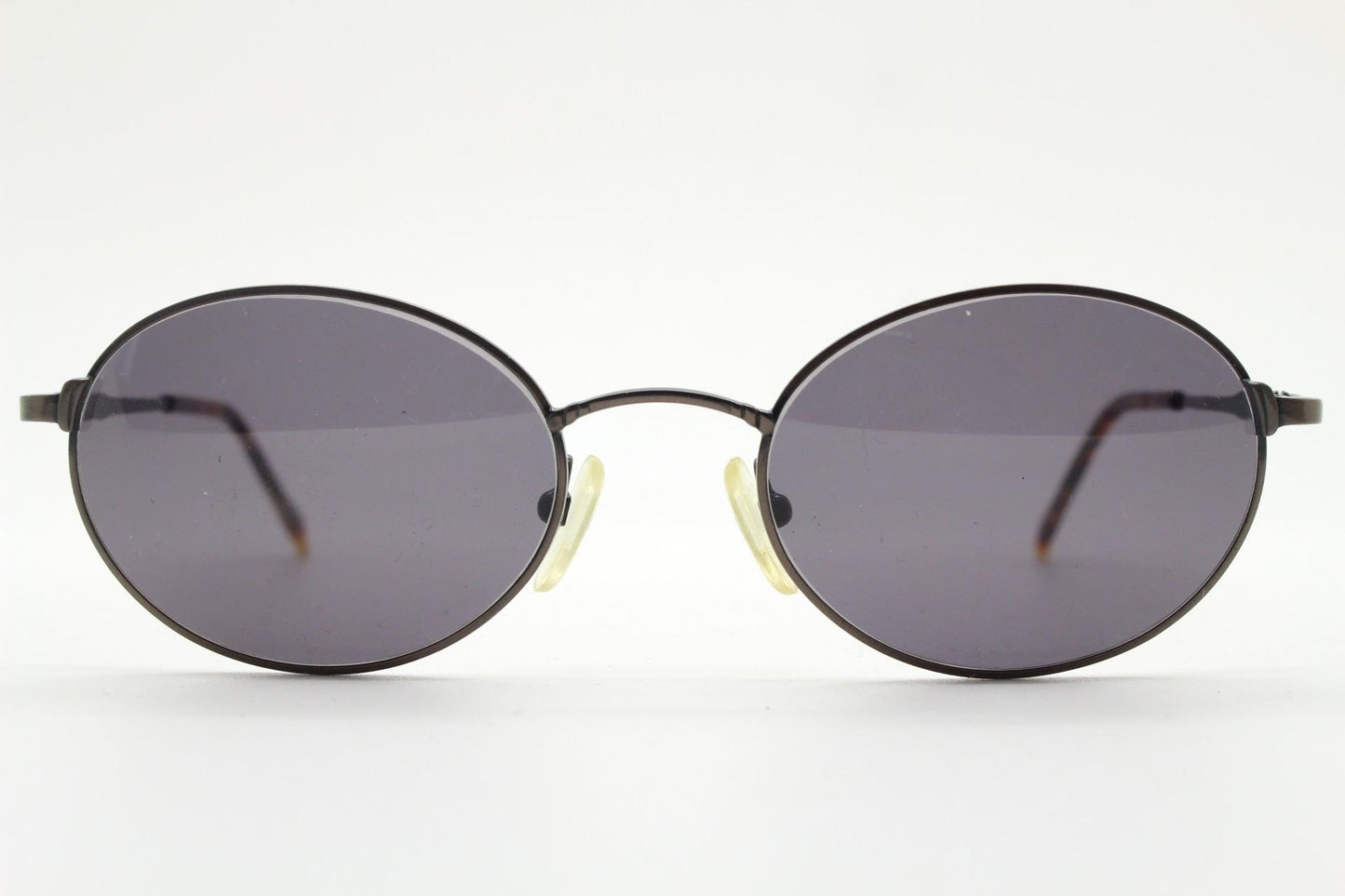90s oval vintage solid metal sunglasses by Sunex. Minimal gloss finish bronze brown frame with grey lenses and subtle arm detail. Unused NOS
