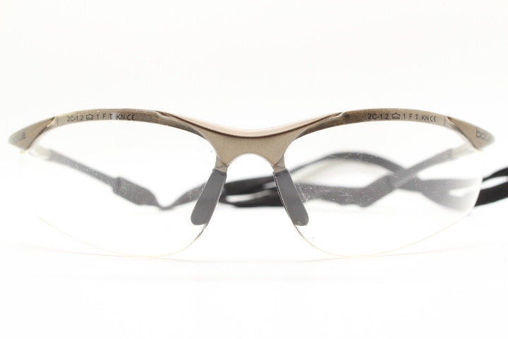 Bolle 90s vintage sports shield sunglasses. Aerodynamic clear lens wrap around half frame design in satin finish with tie string. Cycling