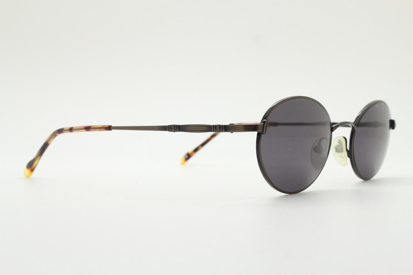 90s oval vintage solid metal sunglasses by Sunex. Minimal gloss finish bronze brown frame with grey lenses and subtle arm detail. Unused NOS