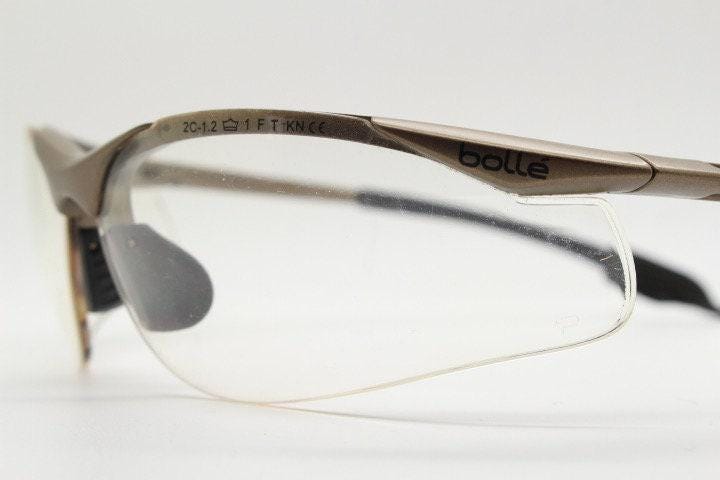 Bolle 90s vintage sports shield sunglasses. Aerodynamic clear lens wrap around half frame design in satin finish with tie string. Cycling