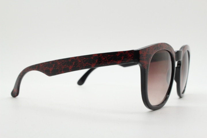 80s vintage rounded wayfarer design sunglasses. Abstract patterned red brow and arms on a black frame with graduating  lenses. Unused NOS