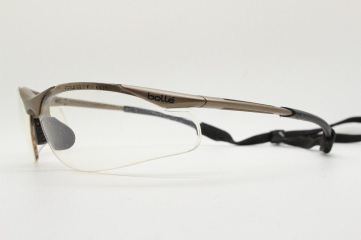 Bolle 90s vintage sports shield sunglasses. Aerodynamic clear lens wrap around half frame design in satin finish with tie string. Cycling