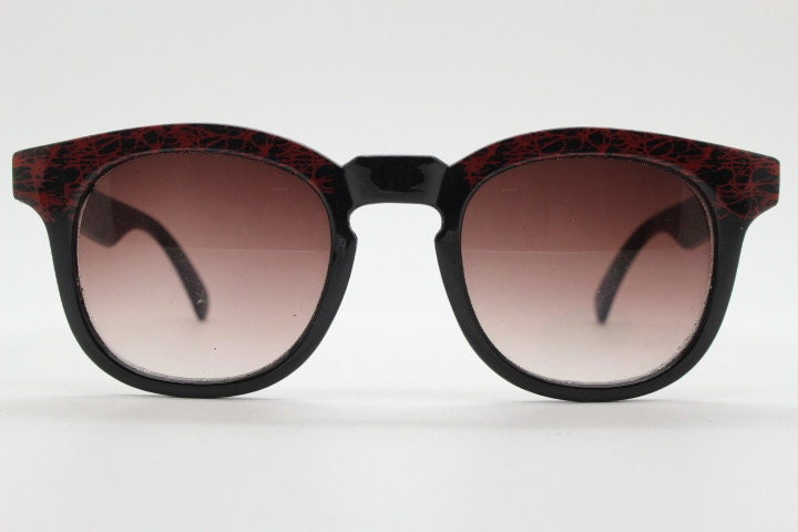 80s vintage rounded wayfarer design sunglasses. Abstract patterned red brow and arms on a black frame with graduating  lenses. Unused NOS