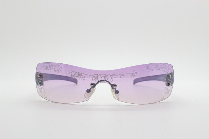 Y2K vintage visor sunglasses. Frameless 2000's purple wraparound mini mask shield design with light tone mono lens and flower print. 00s NOS