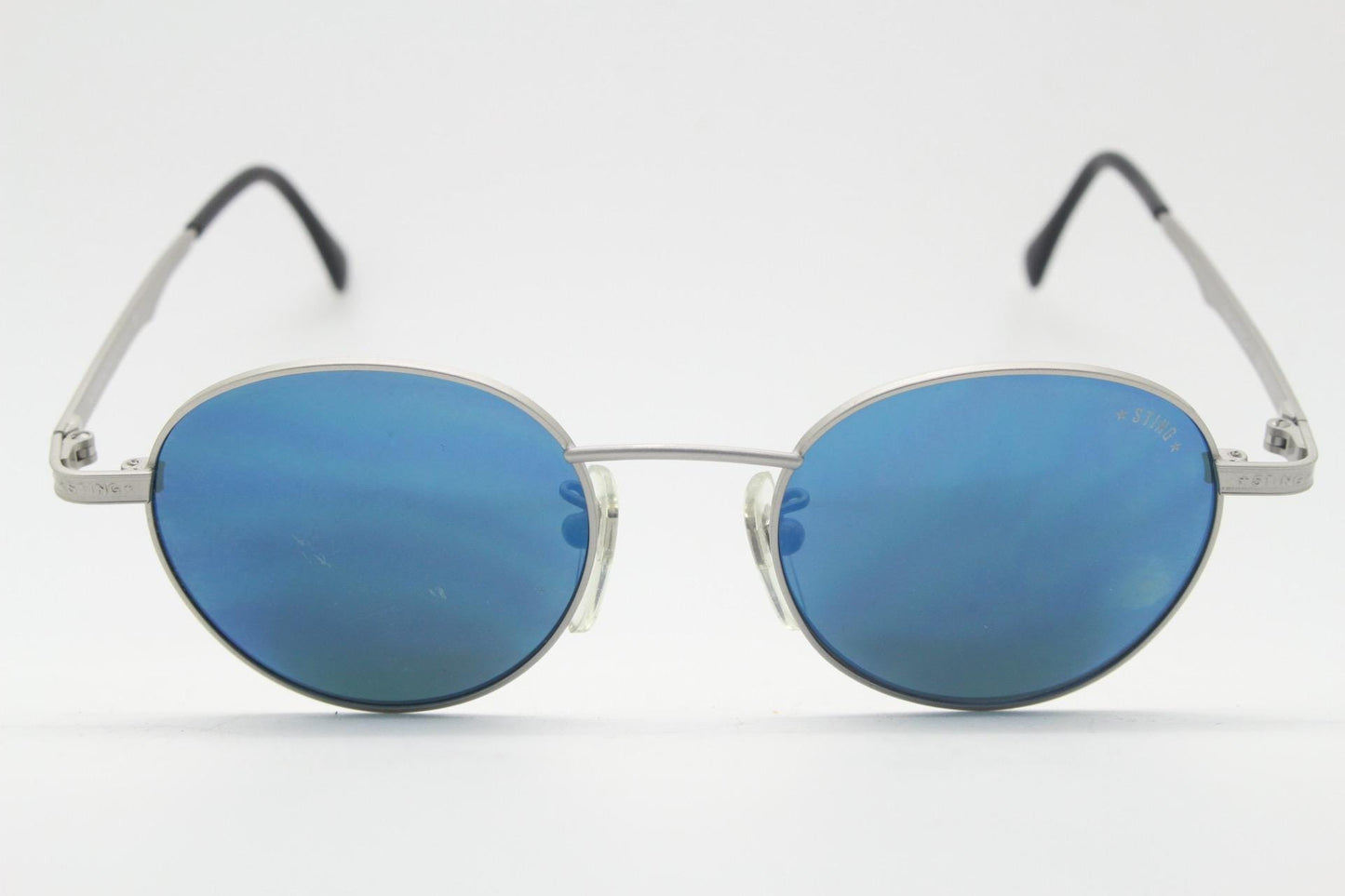 Sting 90s vintage oval sunglasses made in Italy. Minimal grey aluminium look in slightly small proportions with blue mirror lenses