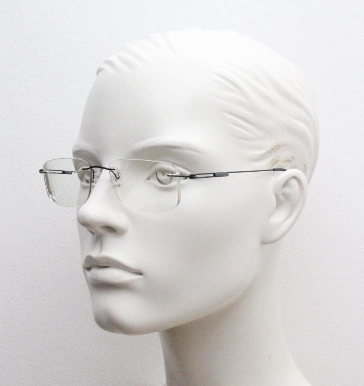 A mannequin head wearing a pair of rimless, wire-rimmed glasses against a plain white background.