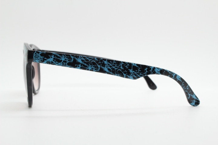 80s vintage rounded wayfarer design sunglasses. Abstract patterned blue brow and arms on a black frame with graduating  lenses. Unused NOS