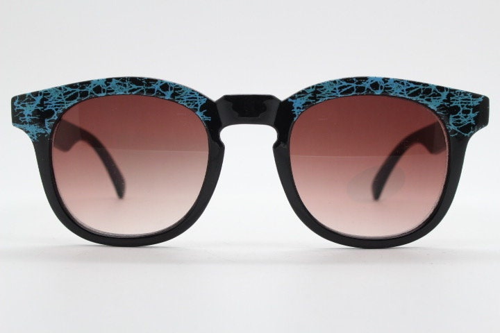 80s vintage rounded wayfarer design sunglasses. Abstract patterned blue brow and arms on a black frame with graduating  lenses. Unused NOS