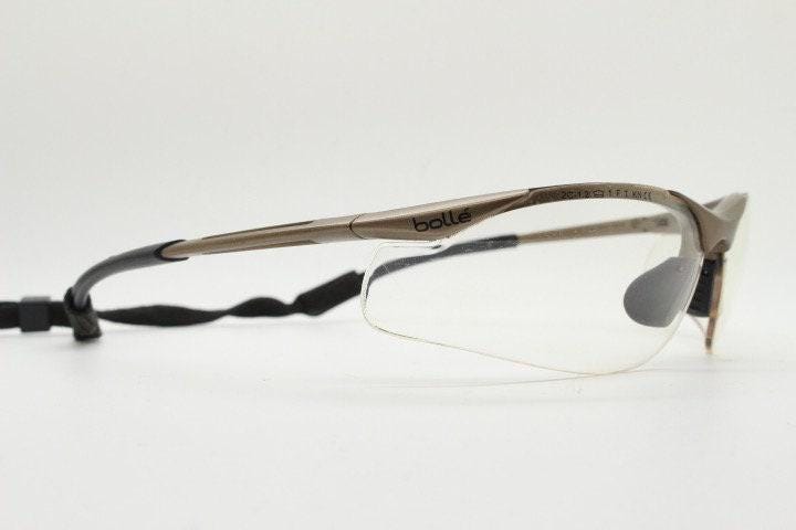 Bolle 90s vintage sports shield sunglasses. Aerodynamic clear lens wrap around half frame design in satin finish with tie string. Cycling
