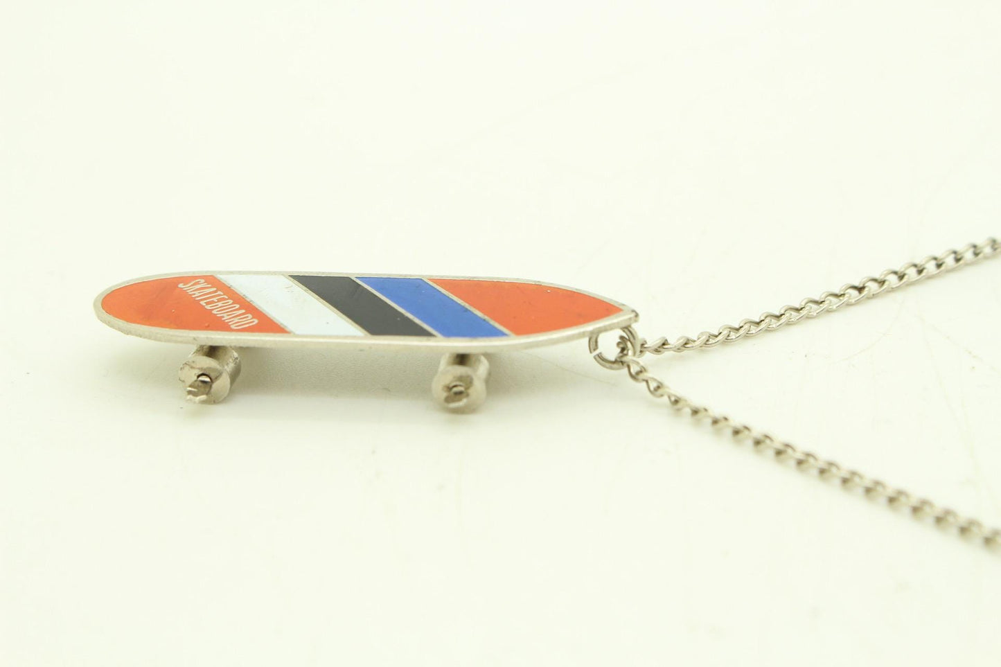 80s vintage skateboard pendant necklace. Metal chrome with enamelled red, blue and white colour stripes. Charming authentic design. NOS