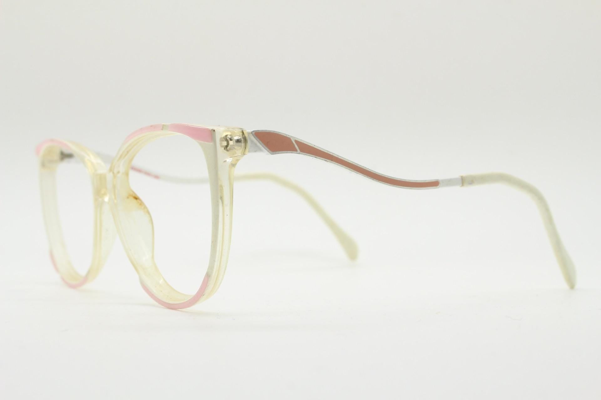 May include: Vintage spectacles with a clear frame, featuring pink and brown accents. The glasses have a rectangular shape and a light-coloured temple arm. The overall design is retro and stylish.