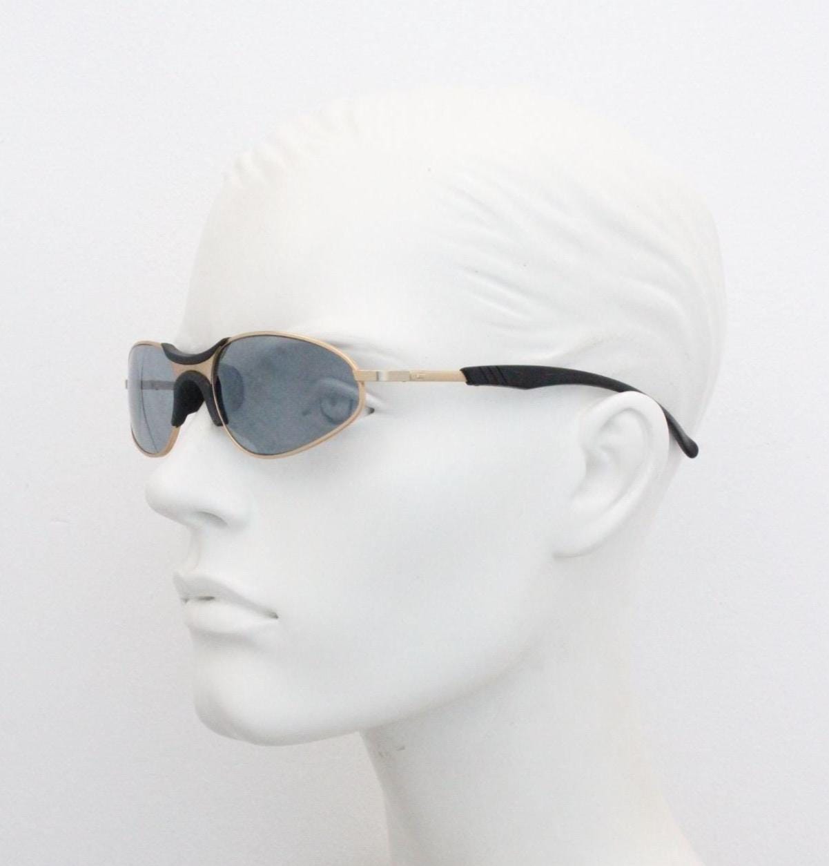 90s vintage oval small bug eye sunglasses. Curved gold satin finish metal frame with black matt trim and adjustable arm length. Unused NOS