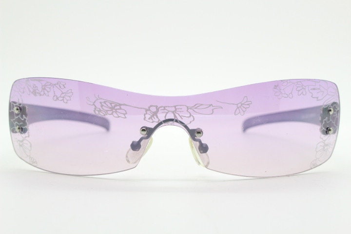 Y2K vintage visor sunglasses. Frameless 2000's purple wraparound mini mask shield design with light tone mono lens and flower print. 00s NOS