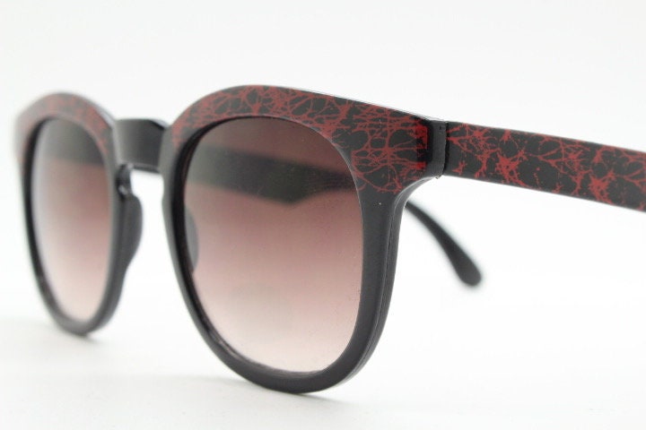 80s vintage rounded wayfarer design sunglasses. Abstract patterned red brow and arms on a black frame with graduating  lenses. Unused NOS