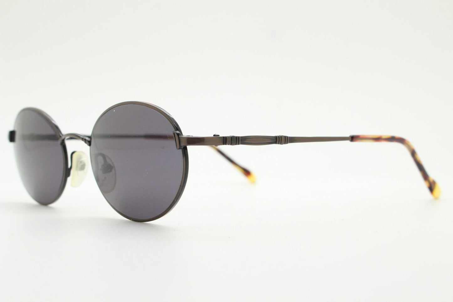 90s oval vintage solid metal sunglasses by Sunex. Minimal gloss finish bronze brown frame with grey lenses and subtle arm detail. Unused NOS