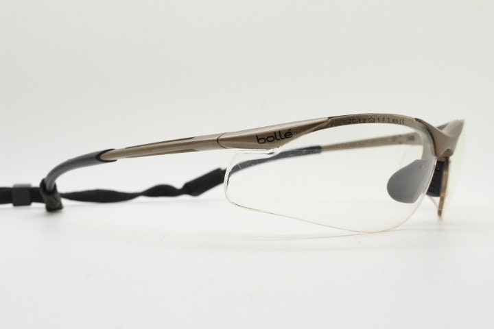 Bolle 90s vintage sports shield sunglasses. Aerodynamic clear lens wrap around half frame design in satin finish with tie string. Cycling