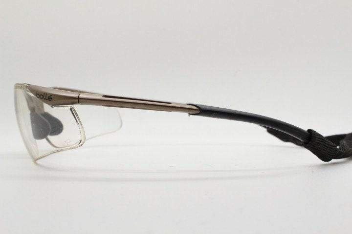 Bolle 90s vintage sports shield sunglasses. Aerodynamic clear lens wrap around half frame design in satin finish with tie string. Cycling