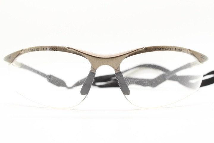 Bolle 90s vintage sports shield sunglasses. Aerodynamic clear lens wrap around half frame design in satin finish with tie string. Cycling