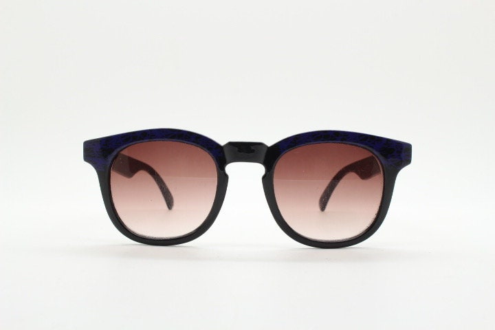 80s vintage rounded wayfarer design sunglasses. Abstract patterned purple brow and arms on a black frame with graduating  lenses. Unused NOS