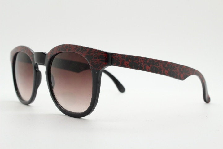 80s vintage rounded wayfarer design sunglasses. Abstract patterned red brow and arms on a black frame with graduating  lenses. Unused NOS