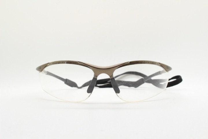 Bolle 90s vintage sports shield sunglasses. Aerodynamic clear lens wrap around half frame design in satin finish with tie string. Cycling