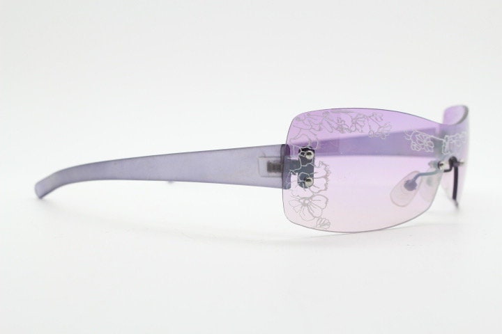 Y2K vintage visor sunglasses. Frameless 2000's purple wraparound mini mask shield design with light tone mono lens and flower print. 00s NOS