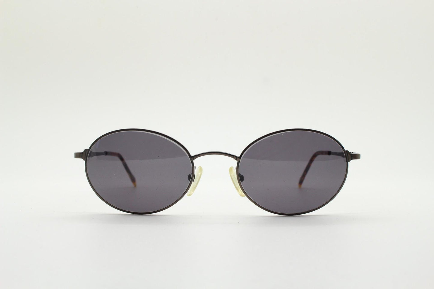 90s oval vintage solid metal sunglasses by Sunex. Minimal gloss finish bronze brown frame with grey lenses and subtle arm detail. Unused NOS