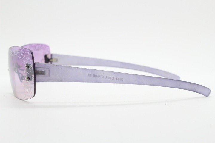 Y2K vintage visor sunglasses. Frameless 2000's purple wraparound mini mask shield design with light tone mono lens and flower print. 00s NOS
