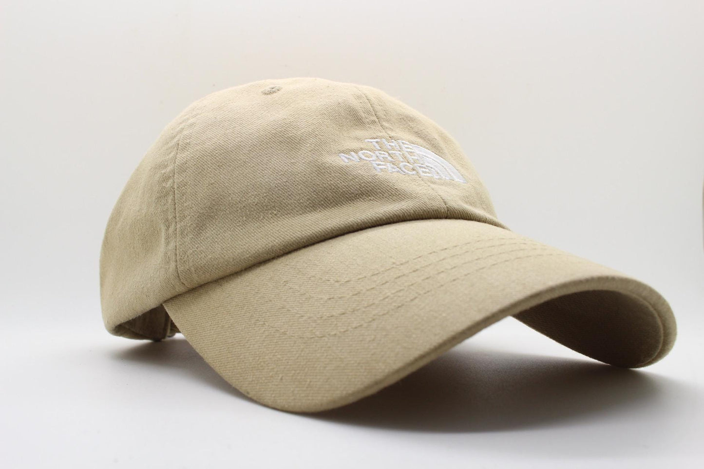 The North Face beige / sand colour baseball cap with white spell out logo. Classic trucker style hat with fully adjustable back. One size