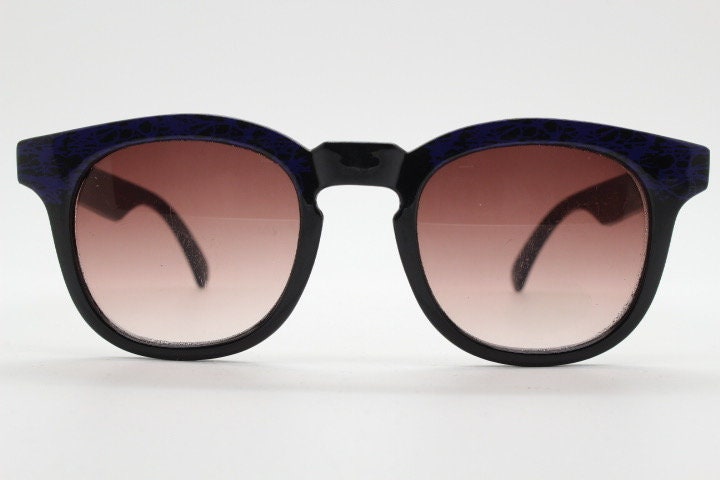80s vintage rounded wayfarer design sunglasses. Abstract patterned purple brow and arms on a black frame with graduating  lenses. Unused NOS