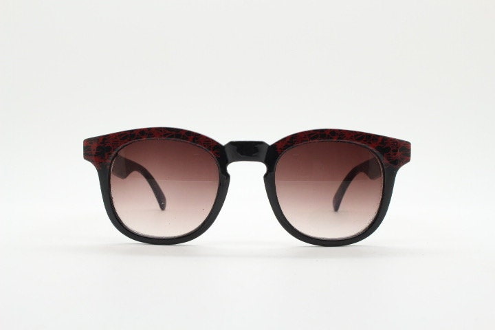80s vintage rounded wayfarer design sunglasses. Abstract patterned red brow and arms on a black frame with graduating  lenses. Unused NOS
